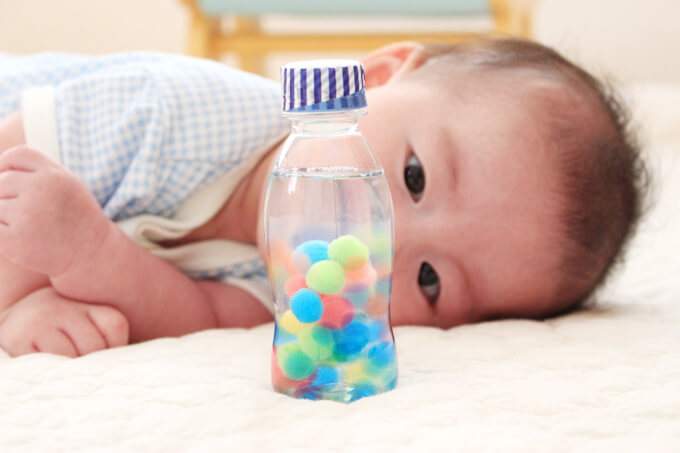 水入りペットボトルガラガラを見つめる3ヶ月の赤ちゃん